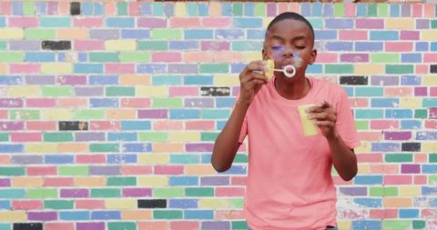 Boy blowing bubbles near vibrant colorful brick wall