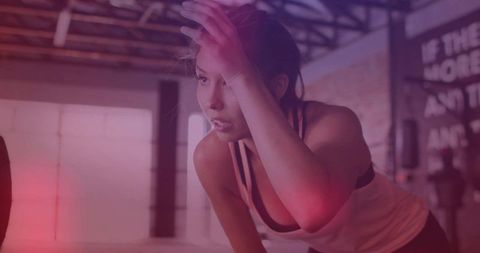 Woman wiping forehead during intense workout in industrial neon warehouse gym