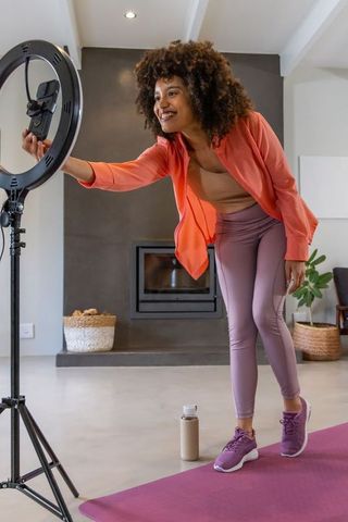 Adjusting phone on ring light for home fitness livestream smiling african american creator