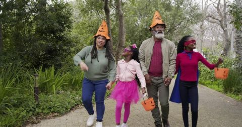 Family walking through park wearing pumpkin hats and carrying halloween buckets
