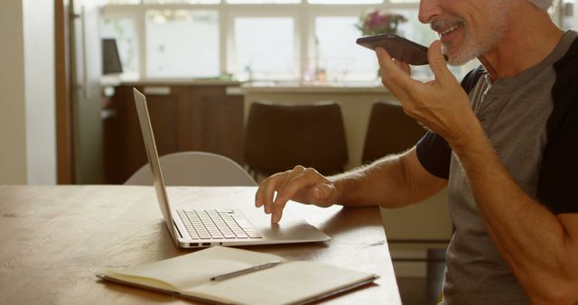 Senior Man Using Voice Assistant on Smartphone While Working on Laptop - Download Free Stock Images Pikwizard.com