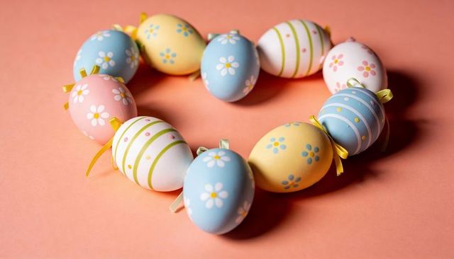 Pastel easter eggs forming heart with daisy patterns and ribbon loops on coral