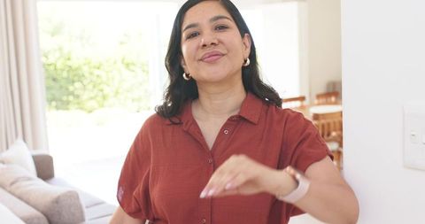 Mid-adult woman reaching toward camera in sunlit modern living room, welcoming gesture
