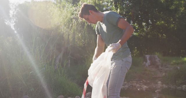 Caucasian male volunteer cleaning up a river on a sunny day in the countryside, picking up rubbish. Ecology and social responsibility in a rural environment.