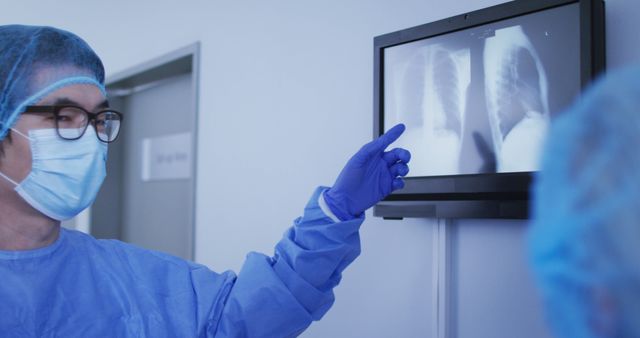 Doctor wearing protective gear analyzing x-ray images on monitor in hospital, ideal for representing healthcare, diagnostic procedures, patient care, medical technology, radiology services, and professional medical scenes in healthcare publications, websites, and marketing materials.