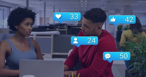 Colleagues discussing social engagement metrics at open office desk with laptop