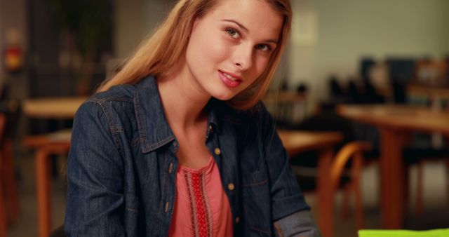 A young Caucasian woman wearing a denim jacket sits casually, with copy space. Her relaxed pose and confident gaze suggest a comfortable setting, a casual meeting or a creative workspace.