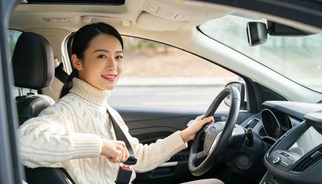 Asian woman fastening seatbelt while smiling in modern car interior with steering wheel