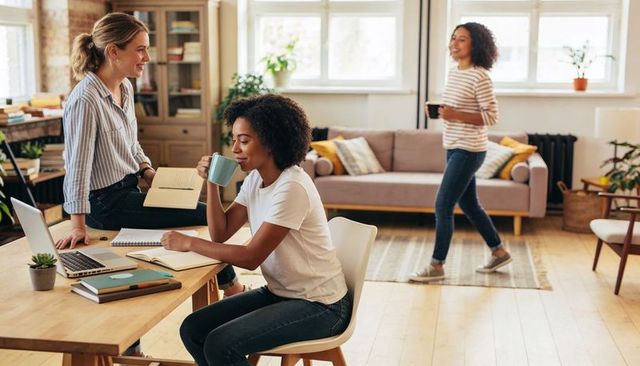 Young women collaborating, working from home office with laptop, notebooks and coffee break