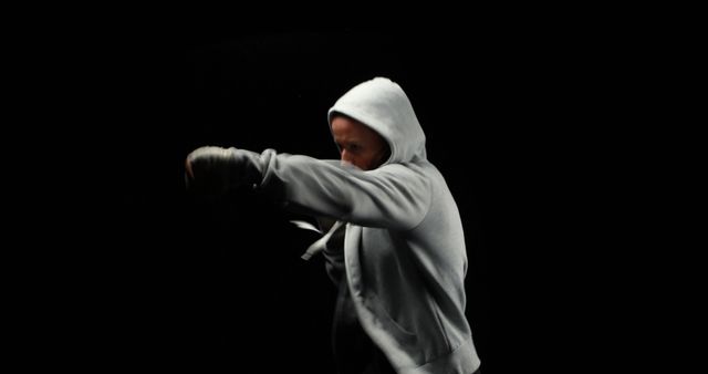 Portrait of focused caucasian female boxer boxing in grey hoodie with copy space on black background. Strength and fitness concept.