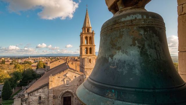 Bronze bell foreground framing historic church tower and terracotta rooftops at sunset