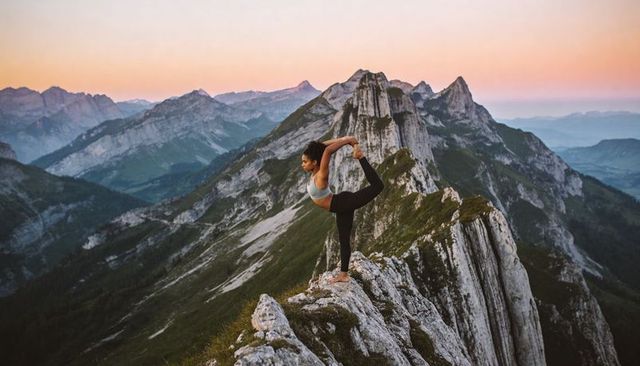 Woman practicing dancer yoga pose on narrow alpine ridge at sunset for mindful fitness
