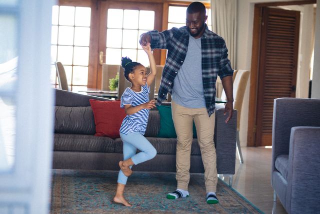 Full length of happy african american father and daughter dancing together in living room at home. unaltered, enjoyment, family, lifestyle and togetherness.
