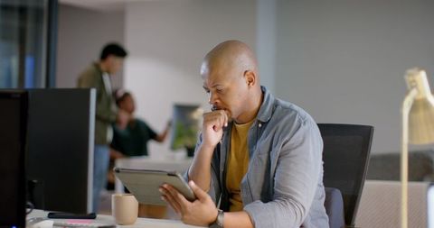 Focused Asian Man Using Tablet in Modern Office Workspace with Coffee and Minimalist Desk