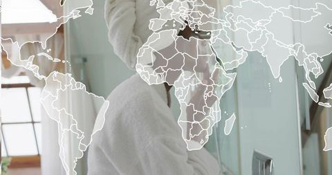 Woman applying skincare at bathroom vanity with towel turban and world map overlay