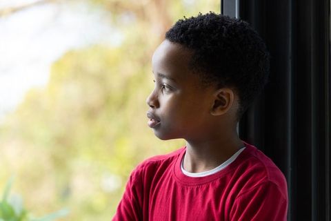 Boy gazing out window side profile thoughtful portrait natural light soft garden bokeh