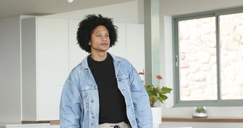 Mid-adult man standing in modern bright kitchen wearing denim jacket and drawstring pants