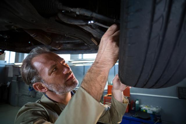 Mechanic inspecting car tire in auto repair shop, ideal for illustrating automotive repair services, vehicle maintenance, and professional mechanic work. Suitable for use in advertisements, brochures, websites, and articles related to car repair and maintenance.