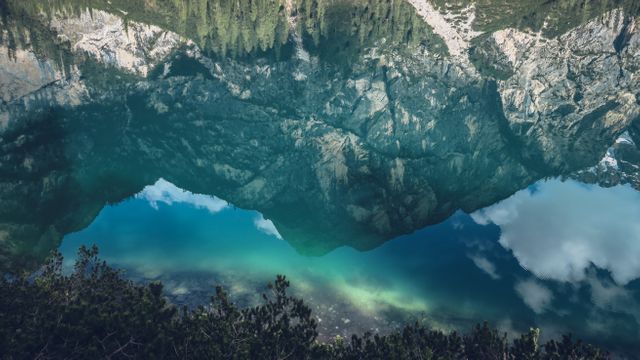 Clear lake reflects dense forest and rugged mountains under a cloudy sky. Suitable for nature blogs, travel magazines, outdoor adventure advertisements, scenic wallpaper.