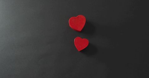 Two red heart blocks resting on dark matte surface casting shadows, minimal composition