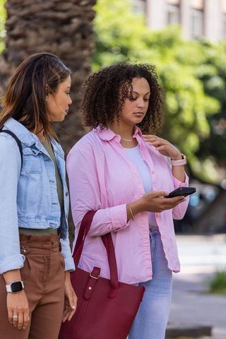 African american friends checking smartphone on urban sidewalk with red tote bag