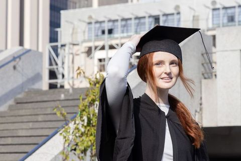 Graduate smiling on campus stairs wearing mortarboard and gown, urban university celebration