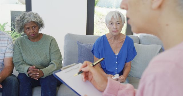 Two elderly women in a group therapy session attentively listening to a therapist with a clipboard. Ideal for illustrating themes of mental health support, senior care, counseling, psychological help, and group therapy dynamics among the elderly.