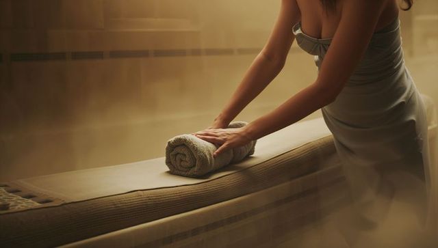 Spa attendant arranging rolled towel on padded treatment table in warm ambient light