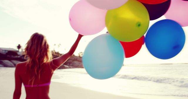 Woman holding colorful balloons while standing on a sunny beach. Ideal for concepts related to summer, vacation, celebration, and carefree moments. Great for tourism ads, lifestyle blogs, and social media content promoting outdoor fun and happiness.