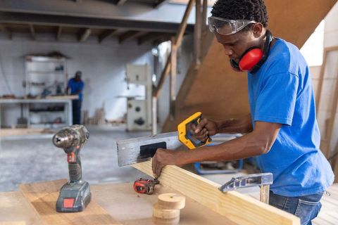 African american carpenter cutting pine board with handsaw in workshop