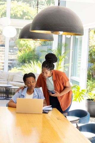 Mother helping daughter with laptop and notebooks in bright modern home learning moment