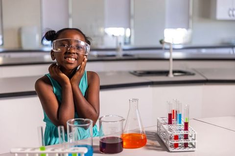 African american girl wearing goggles conducting colorful science experiment in school lab