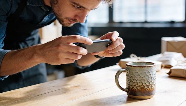 Cafe owner photographing rustic ceramic mug for product listing and social media