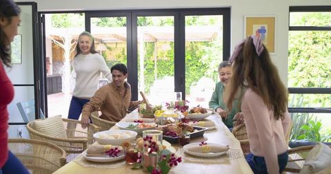 Multigenerational family gathering at sunlit dining table passing bowls and sharing meal