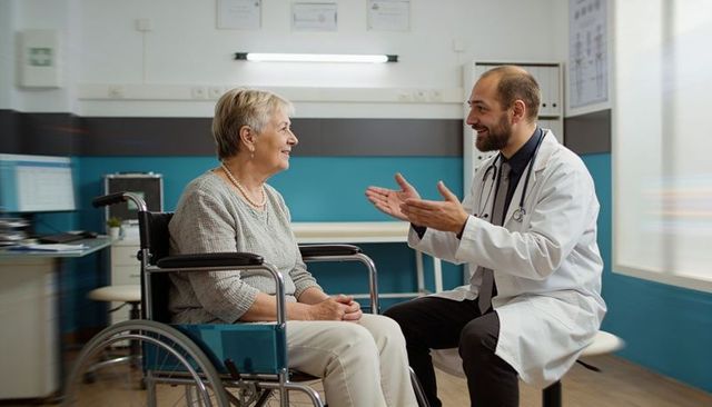 Friendly doctor consulting senior woman in wheelchair during routine medical clinic visit