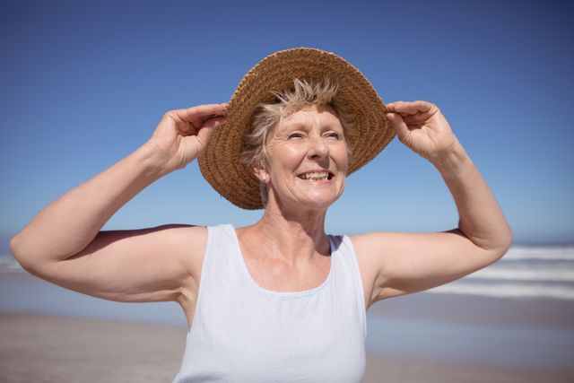 Smiling senior woman wearing sun hat at beach during sunny day