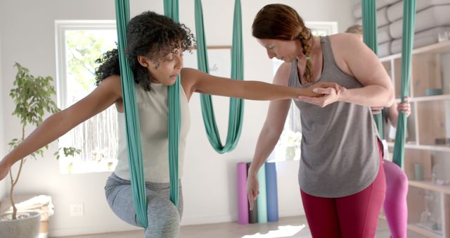Yoga participants using aerial hammocks while instructor provides guidance in relaxed studio environment. Great for content promoting yoga classes, fitness programs, health benefits, relaxation techniques, or wellness workshops.