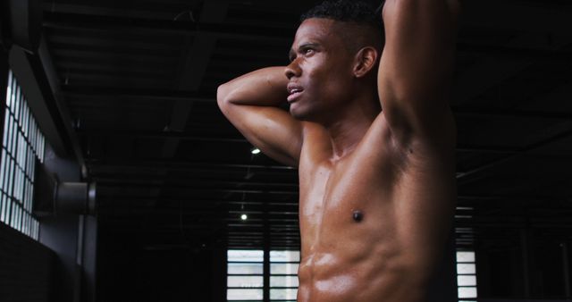 Athletic man stretching in a gym interior, showcasing post-workout perspiration. Suitable for use in fitness blogs, workout programs, sports advertisements, and health magazines.
