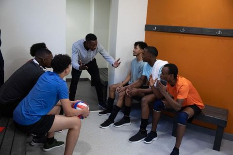 Coach motivating diverse male volleyball team during locker room huddle and strategy talk