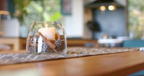 Glowing glass centerpiece creating cozy table ambience with lit candle and pinecones