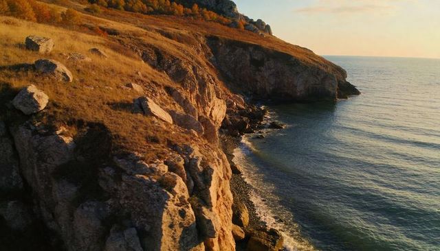 Golden-hour coastal cliff revealing rugged rockface, headland and calm sea