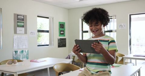 African boy using tablet in bright classroom smiling and learning with technology