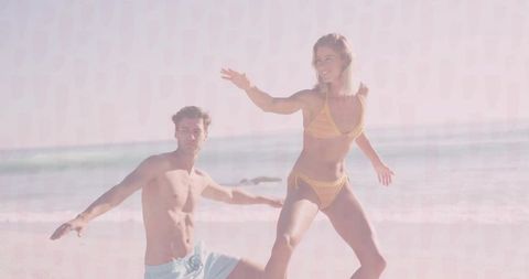 Fit couple balancing on wet sand at ocean edge in sunny yellow bikini and swim trunks