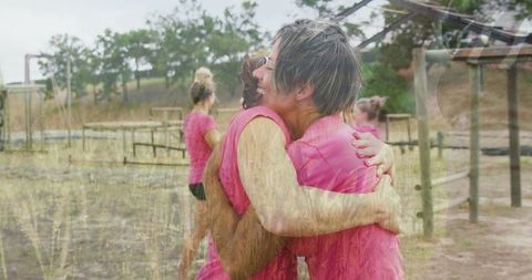 Teammates hugging on outdoor obstacle course in pink athletic wear