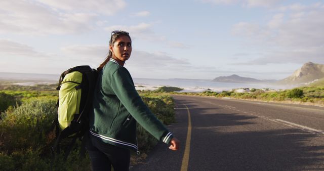 Woman walking down scenic mountain road during sunset, carrying backpack. Ideal for travel blogs, magazines, adventure promotions, and outdoor lifestyle content.