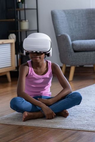 African american girl wearing vr headset sitting cross-legged on rug in modern living room
