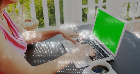 Woman typing on laptop with green screen on sunny porch with coffee and data overlay