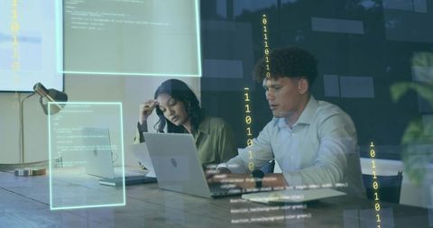 Developers collaborating over code on laptops at modern office table with binary data projections
