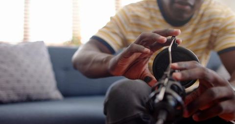 Leaning forward man adjusting microphone and headphones on cozy home studio couch