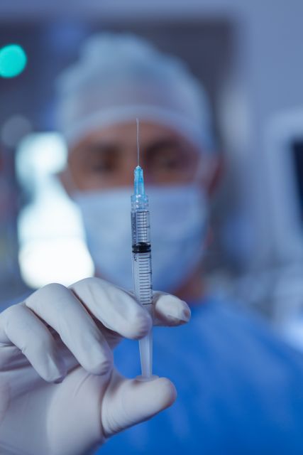 This image shows a close-up of a surgeon holding a syringe in an operating room. The surgeon is wearing gloves and a mask, emphasizing the sterile environment. This image can be used for medical articles, healthcare promotions, surgical procedure explanations, or hospital advertisements.